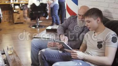 年轻人和成熟男人使用数码平板电脑，在理发店等待轮到他们